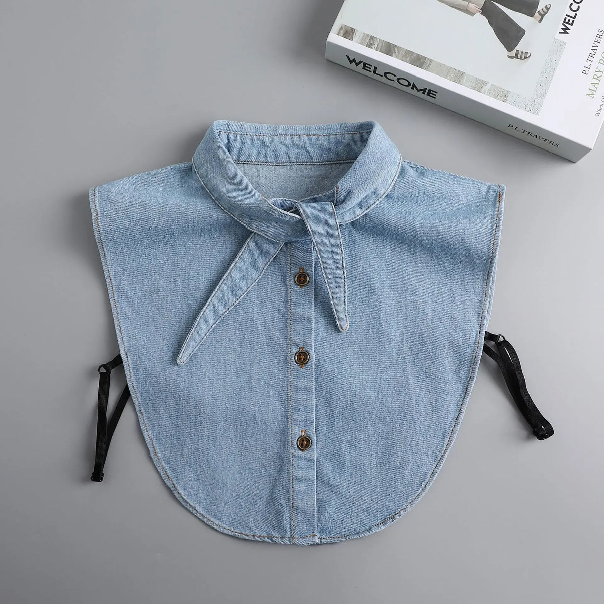 A light blue denim blouse with a false collar detail and buttons is displayed on a gray background.