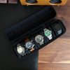 A black leather watch travel case organizer holding several wristwatches and a smartphone on a wooden surface.