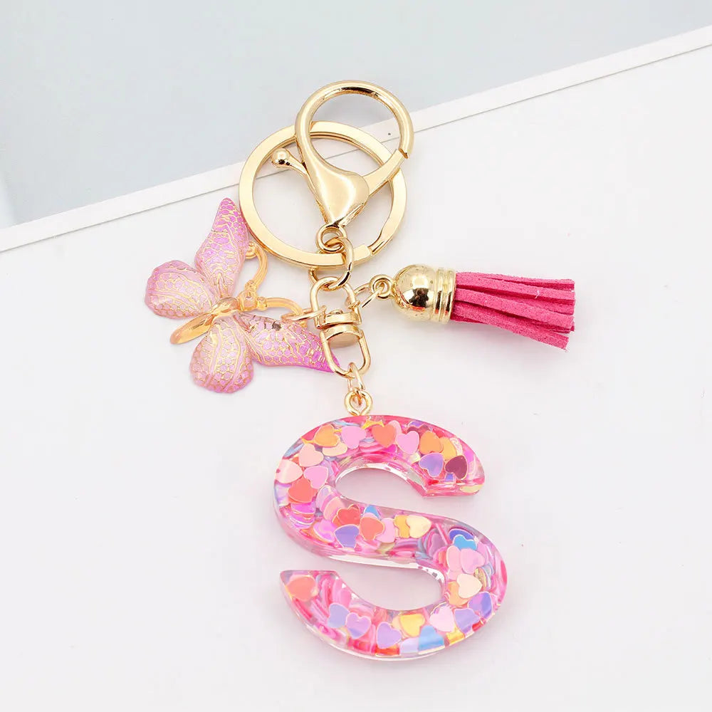 Gold acrylic letter keychain shaped like the letter S with pink glitter and a pink butterfly tassel
