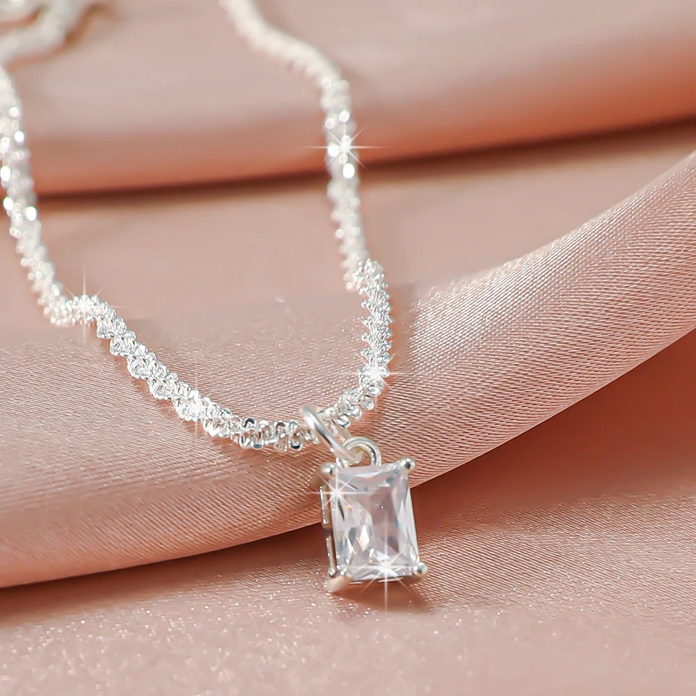 A delicate silver-plated chain necklace with sparkling CZ stones and a rectangular pendant resting on pink fabric.