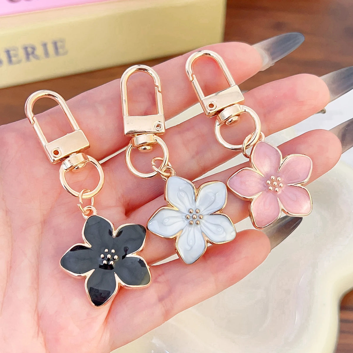 Una mano sostiene un set de llaveros florales dorados con detalles en rosa y blanco.