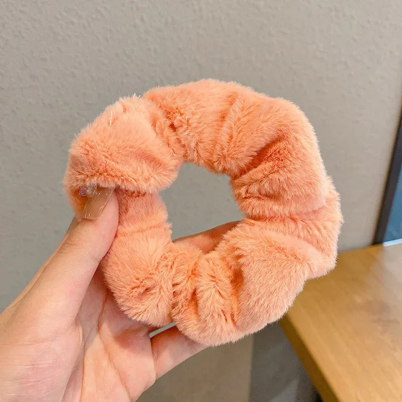 Une main tient un élastique pour cheveux en tricot moelleux orange, montrant sa texture et sa couleur.