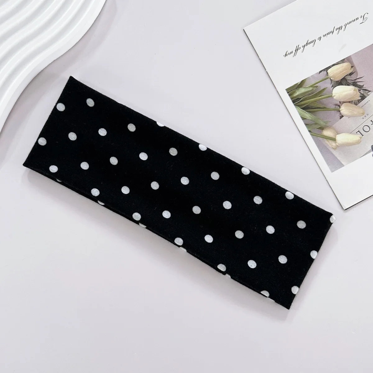 Black fabric hairband with white polka dots lying on a white surface.