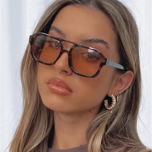 A close-up photo of a woman wearing vintage pilot sunglasses with an orange lens and double bridge.