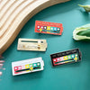 Drei schiebbare Stimmungsbatterie-Pins in rot, gold und schwarz auf einem türkisfarbenen Untergrund.