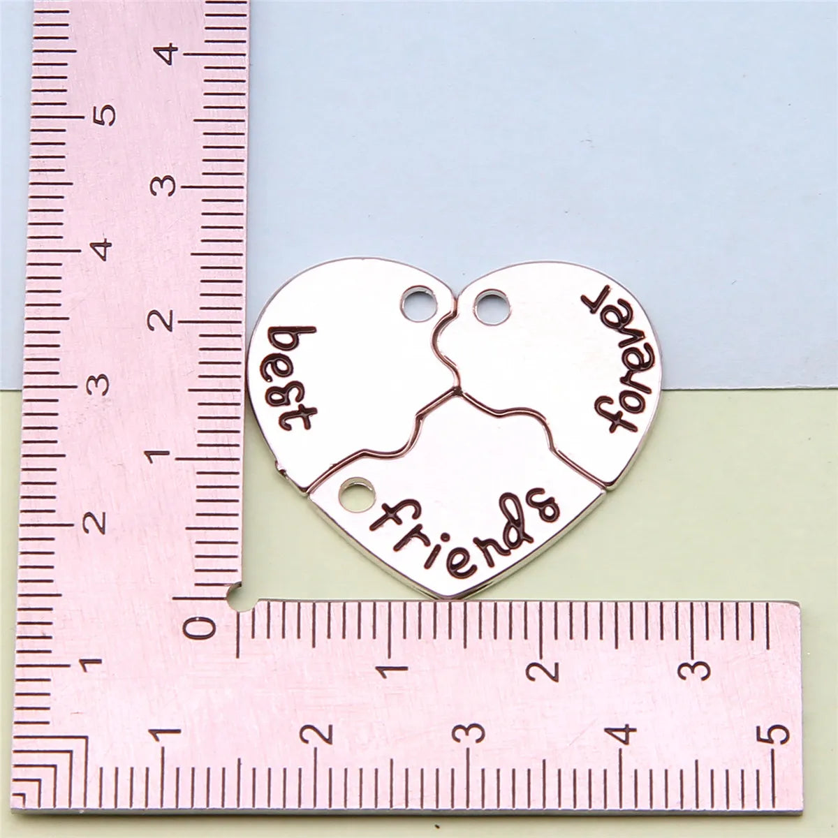 Colgante de corazón plateado con las palabras 'mejores amigos y para siempre', medido contra una regla.