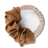 A heatless hair curling scrunchie in a dusty rose or nude fabric, shown as a wide, ruffled band.