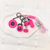 A set of pink fitness keychains and weightlifting accessories including a fitness disc and dumbbells on a white surface.
