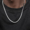 A close-up of a men's stainless steel hip hop Cuban chain necklace worn around the neck against a black shirt.