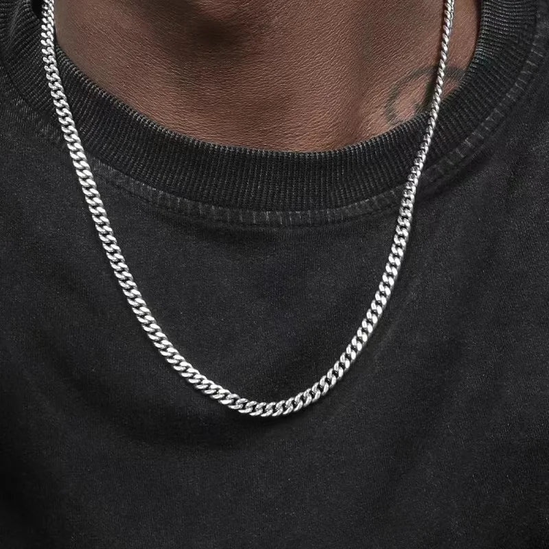 A close-up of a men's stainless steel hip hop Cuban chain necklace worn around the neck against a black shirt.