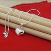 A silver heart snake necklace is displayed on a red velvet fabric next to a wooden surface.