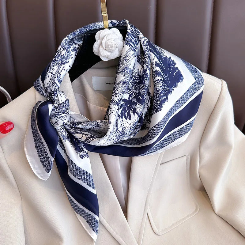 A silk scarf with a blue and white floral print is tied around the neck, displayed against a beige blazer.