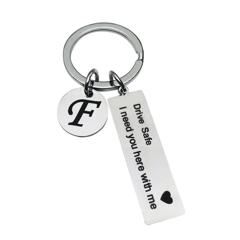 Silver keychain with a circular initial F charm and a rectangular tag that reads Drive Safe I need you here with me
