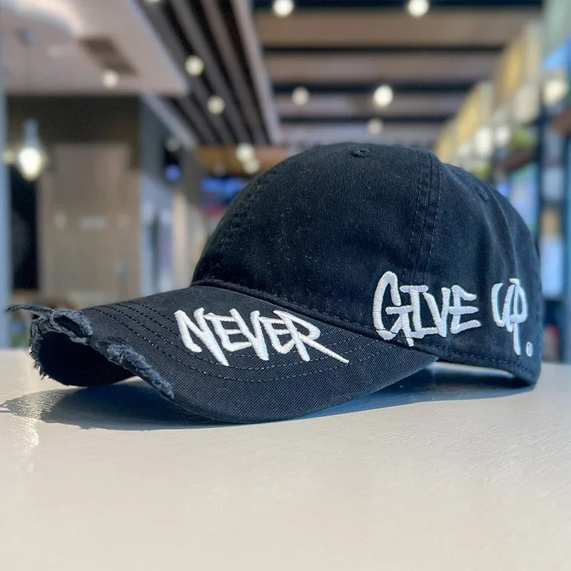 A dark baseball cap with the word NEVER and GIVE UP embroidered on the front, resting on a light surface.