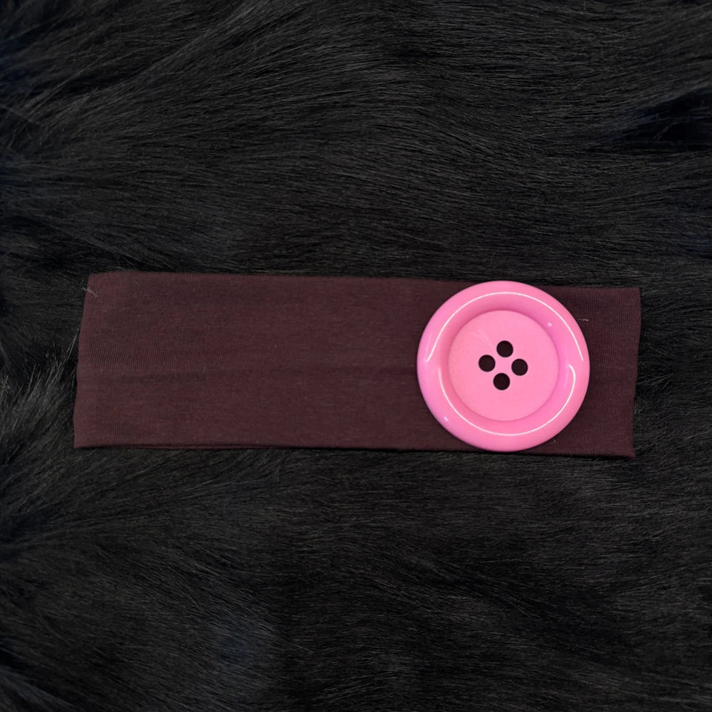 A vintage polka dot button headband in a dark plum color resting on black fur.