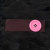 A pink wind dot stretch hairband is shown against a dark brown fabric background.