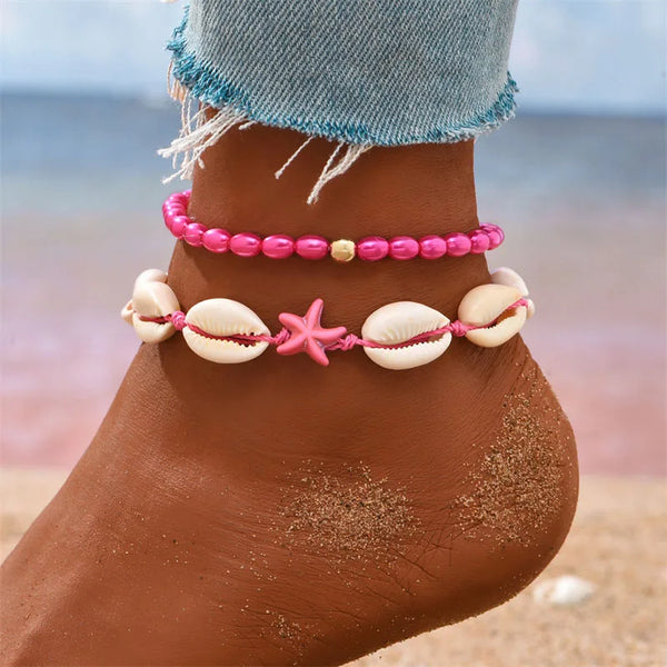 Pink beaded starfish conch anklet worn on a foot against a beach background.