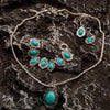 Silver jewelry set featuring turquoise stones including a necklace, earrings, and bracelet displayed on dark rock.