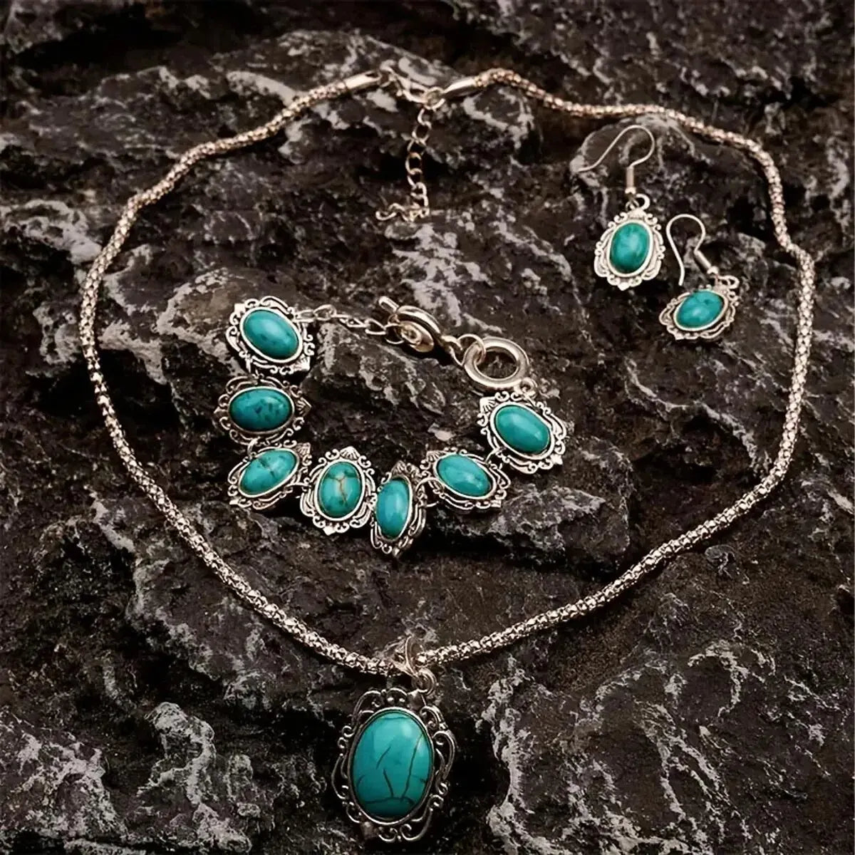 Silver jewelry set featuring turquoise stones including a necklace, earrings, and bracelet displayed on dark rock.
