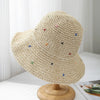Sombrero de paja panama tejido a mano beige con bordado floral colorido, exhibido en un soporte de madera.