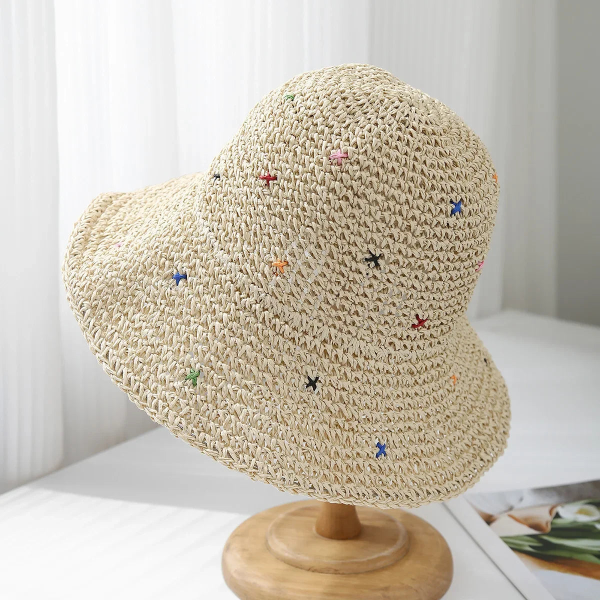 Sombrero de paja panama tejido a mano beige con bordado floral colorido, exhibido en un soporte de madera.