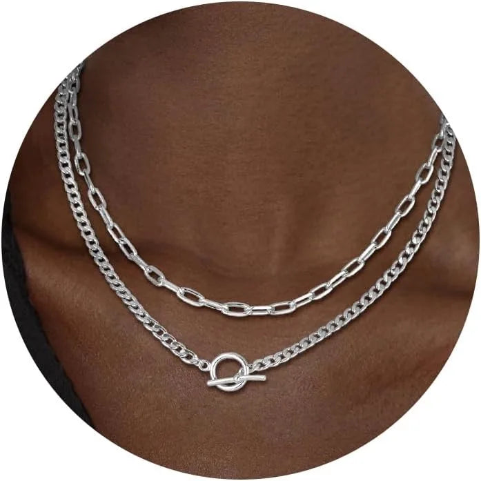 A close-up of a gold layered Cuban link necklace displayed against a brown skin tone.