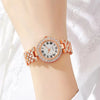 A close-up of a rose gold wristwatch with a white face and pink enamel accents and a rhinestone heart-shaped bracelet on a wr