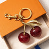 A gold-colored key chain decoration shaped like a leaf and an apple, set inside an orange box.