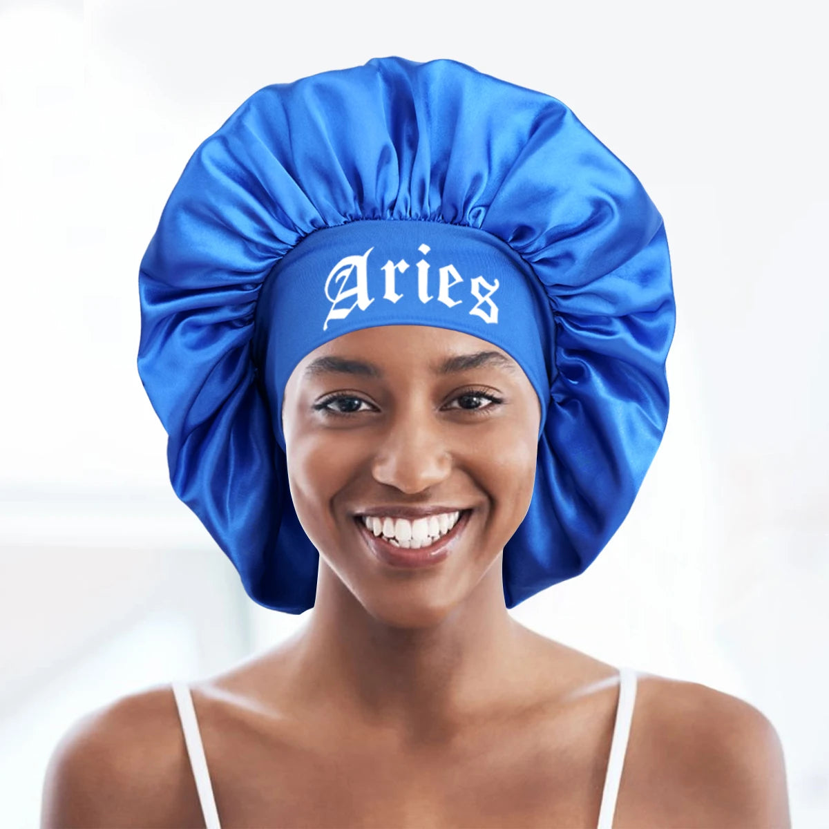 A smiling woman wearing a blue satin sleep bonnet with an Aries wrap band.