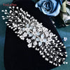 A delicate white rhinestone bridal headband or tiara displayed on a dark velvet fabric next to blue roses.