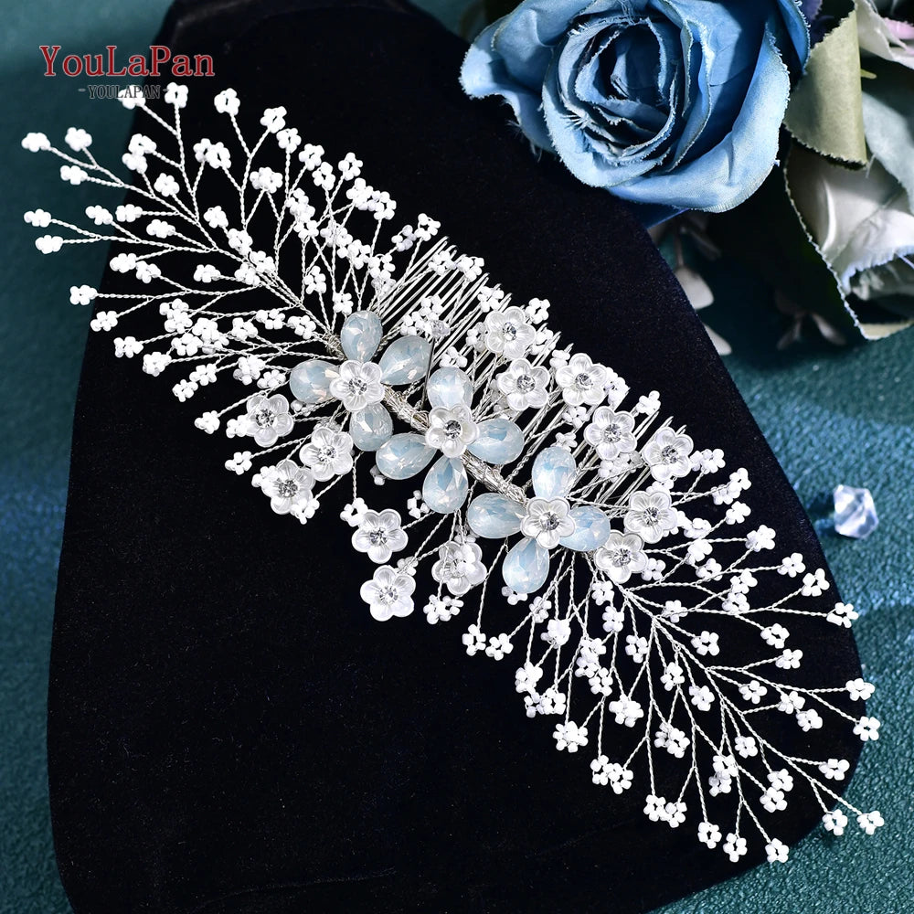 A delicate white rhinestone bridal headband or tiara displayed on a dark velvet fabric next to blue roses.