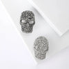 Un par de broches calavera de stras plateados exhibidas sobre un fondo blanco.
