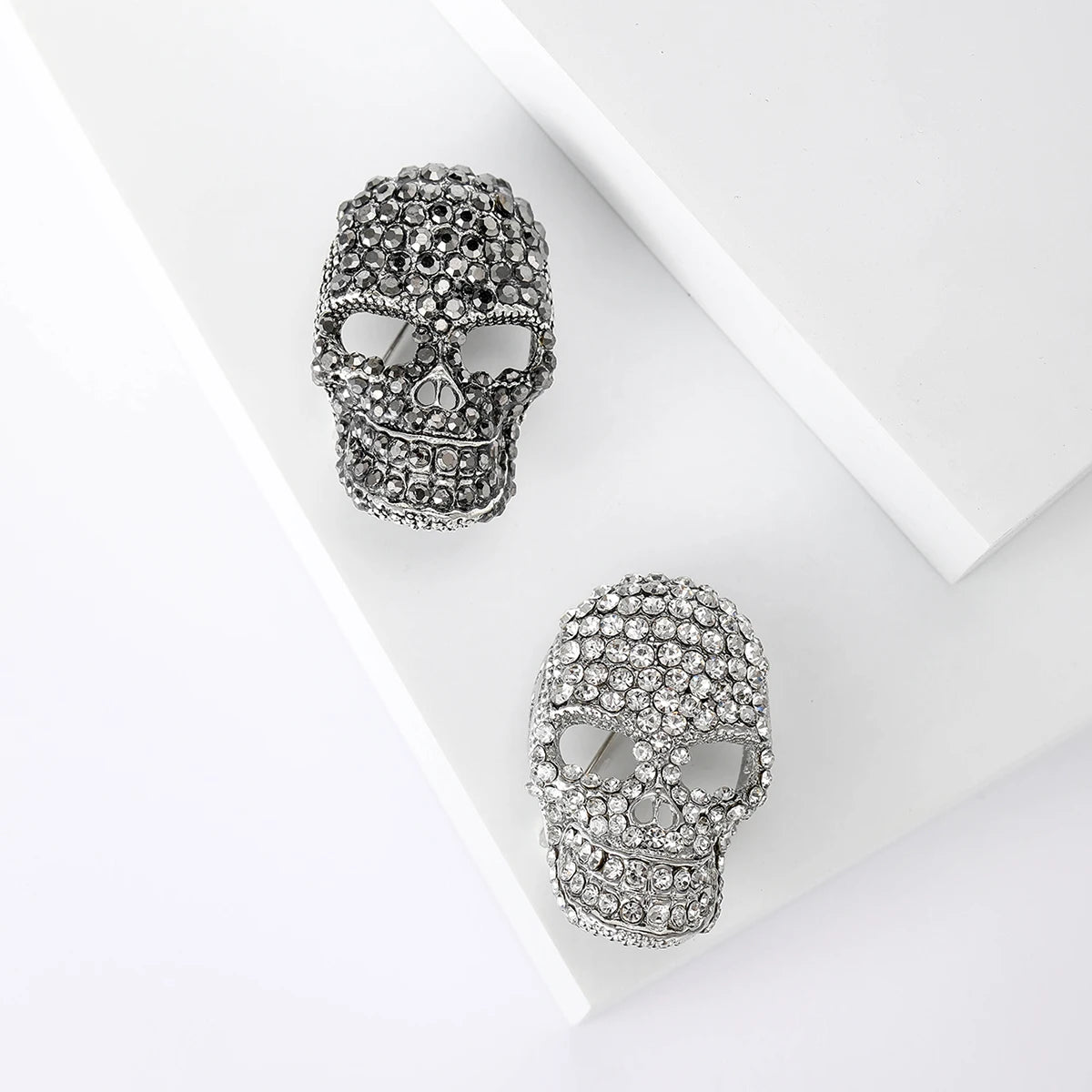 Un par de broches calavera de stras plateados exhibidas sobre un fondo blanco.