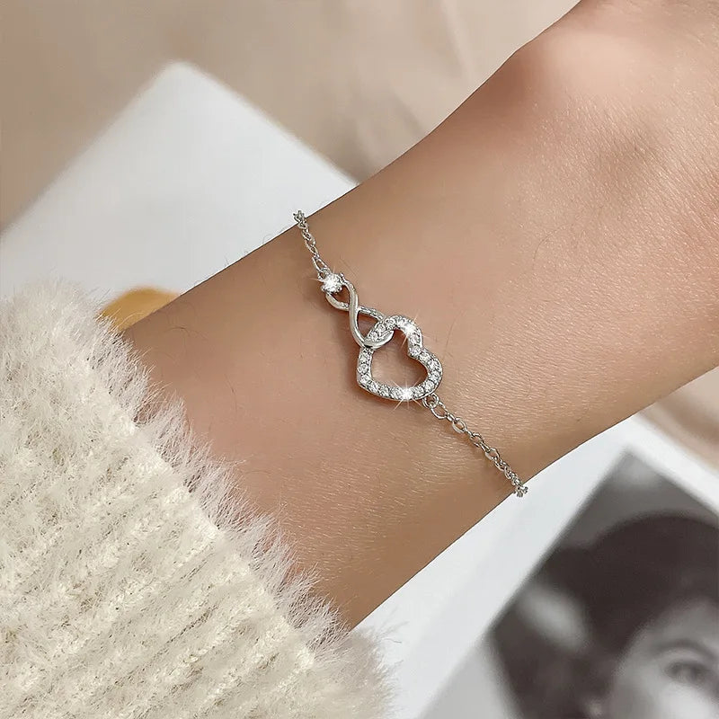 A sterling silver double heart charm bracelet worn on a wrist, next to a fuzzy white sweater.
