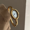 A hand holds a gold-toned vintage quartz analog watch with an oval face and Roman numerals.
