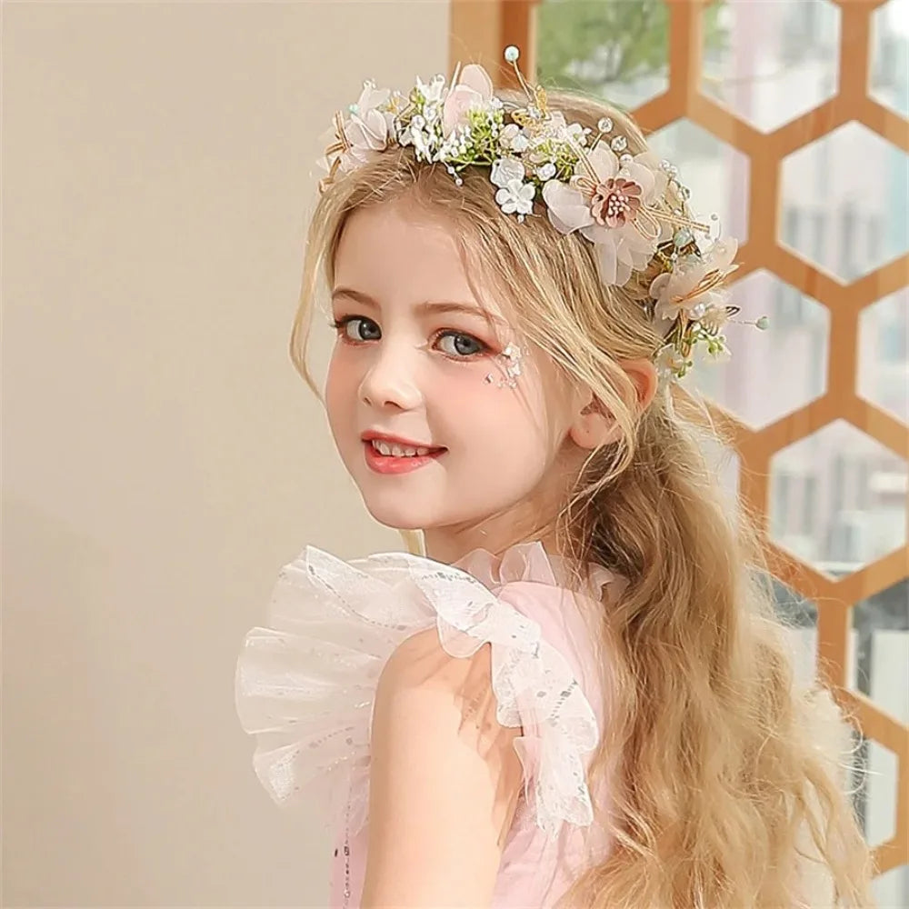 A young girl with long blonde hair wears an elegant floral wreath headband and a pink dress.