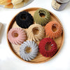 A collection of elegant horsetail hair clips in various shades of black, green, beige, pink, and orange arranged on a wooden 