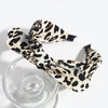 A leopard print retro bow hairband tied in a bow, resting on a clear glass.