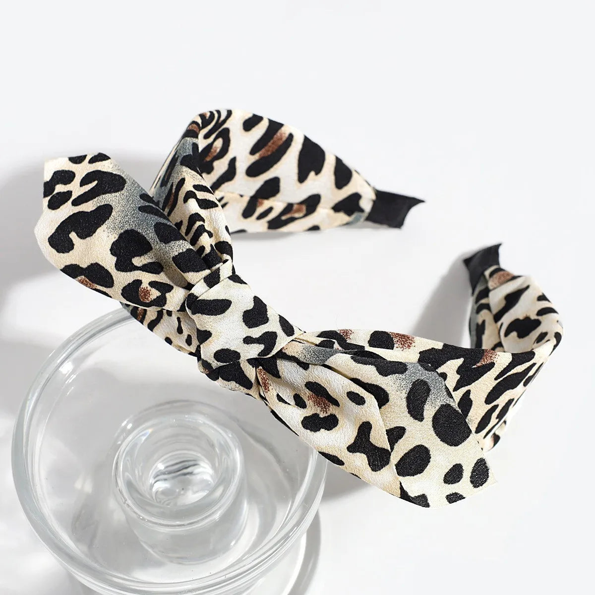 A leopard print retro bow hairband tied in a bow, resting on a clear glass.