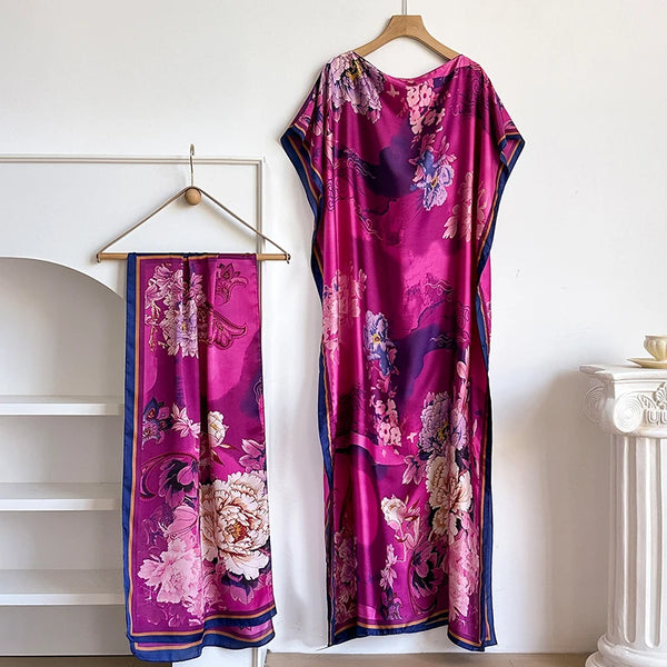 A vibrant magenta floral maxi kaftan dress hanging on a wooden hanger against a white wall.