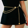 A black dress is worn with a gold chain belt featuring a crystal diamond design.