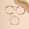 A set of bohemian anklets featuring gold chains and beads in white, red, and teal colors.