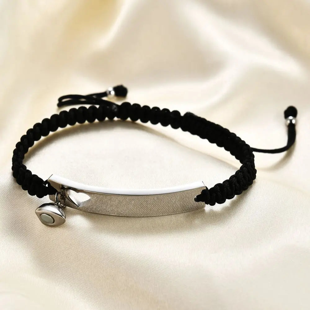 Schwarzer Perlenarmband mit silberner Edelstahlplatte und Anhänger auf cremefarbigem Stoff.