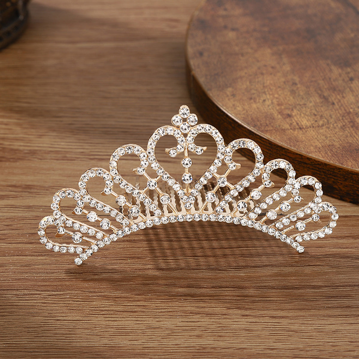 A sparkling crystal princess tiara hair comb for women displayed on a wooden surface.