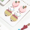 Colección de pendientes colgantes en forma de corazón rosa y amarillo con diversos patrones y detalles dorados, mostrados sob