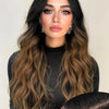 A woman with long wavy brown hair wearing a black turtleneck top.