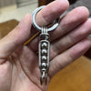 Une main tient un porte-clés mécanique en acier inoxydable avec un anneau et un pendentif décoratif.