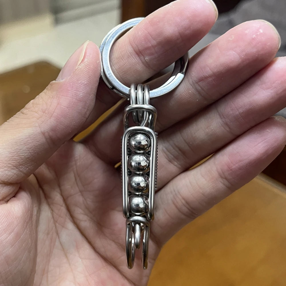 Une main tient un porte-clés mécanique en acier inoxydable avec un anneau et un pendentif décoratif.