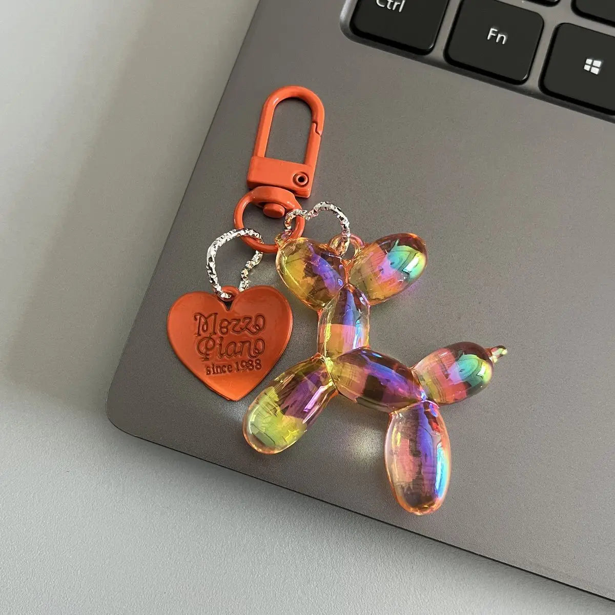 An orange resin animal dog keychain with a silver chain attached to a carabiner, resting on a gray laptop.