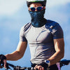 A man wearing sunglasses and a dark balaclava cap is riding a bicycle outdoors.